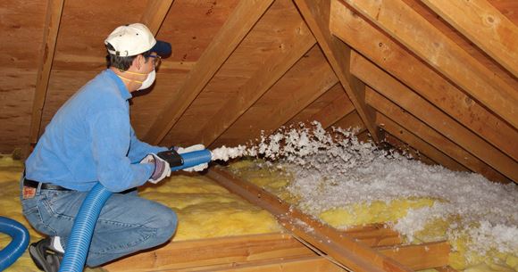 Technician installing blown-in fiberglass insulation in an attic.