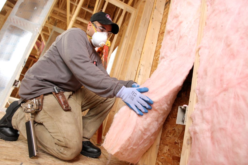 Technician installing fiberglass batting insulation in a wall