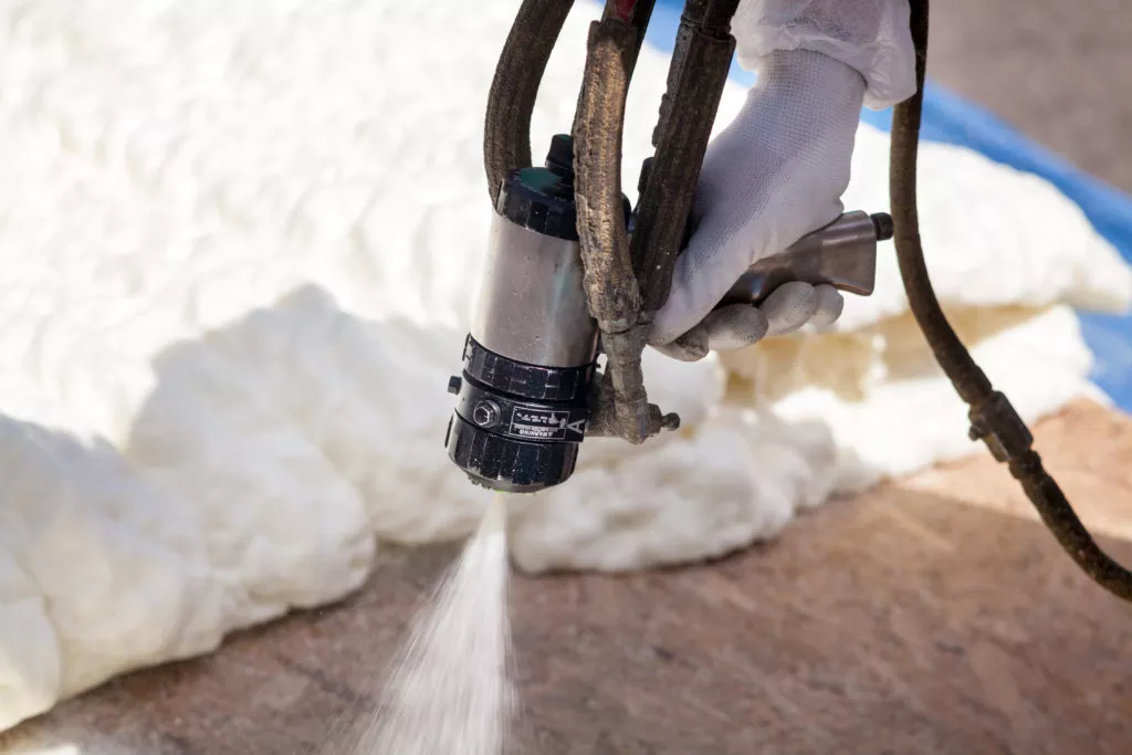 Technician spraying foam insulation using Plural Component Spray Gun.