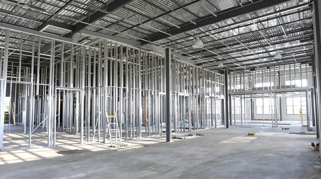 Interior construction site showing metal stud framing installation, galvanized steel profiles